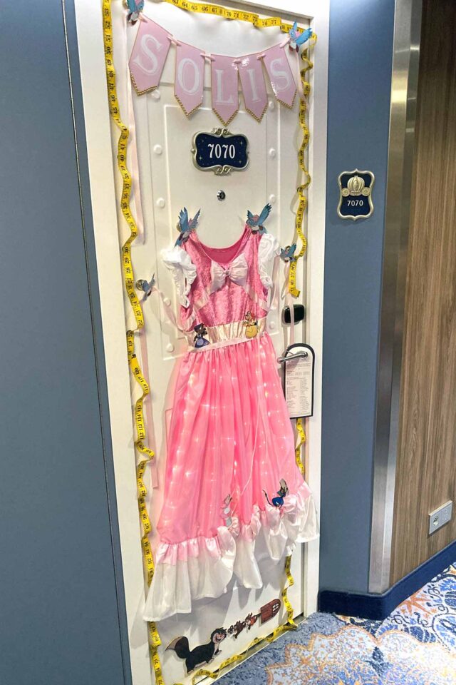 Stateroom door with a pink, fabric Cinderella dress being held at each shoulder by bluebirds