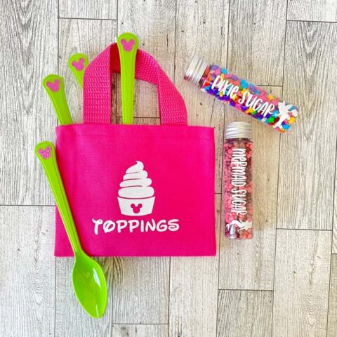 A small pink bag with an ice cream design that reads "toppings. The bag includes four Mickey icon spoons and candy sprinkle toppings.