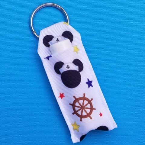 A white lip balm holder with a Disney Cruise Mickey icon and ship's wheel, attached by a keyring holder