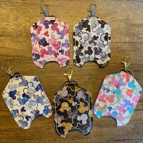 5 hand sanitizer holders, with a clip, decorated with Mickey Mouse icons. Colors are pink and white, black and white, blue and white, silver and gold and black, and pastels.