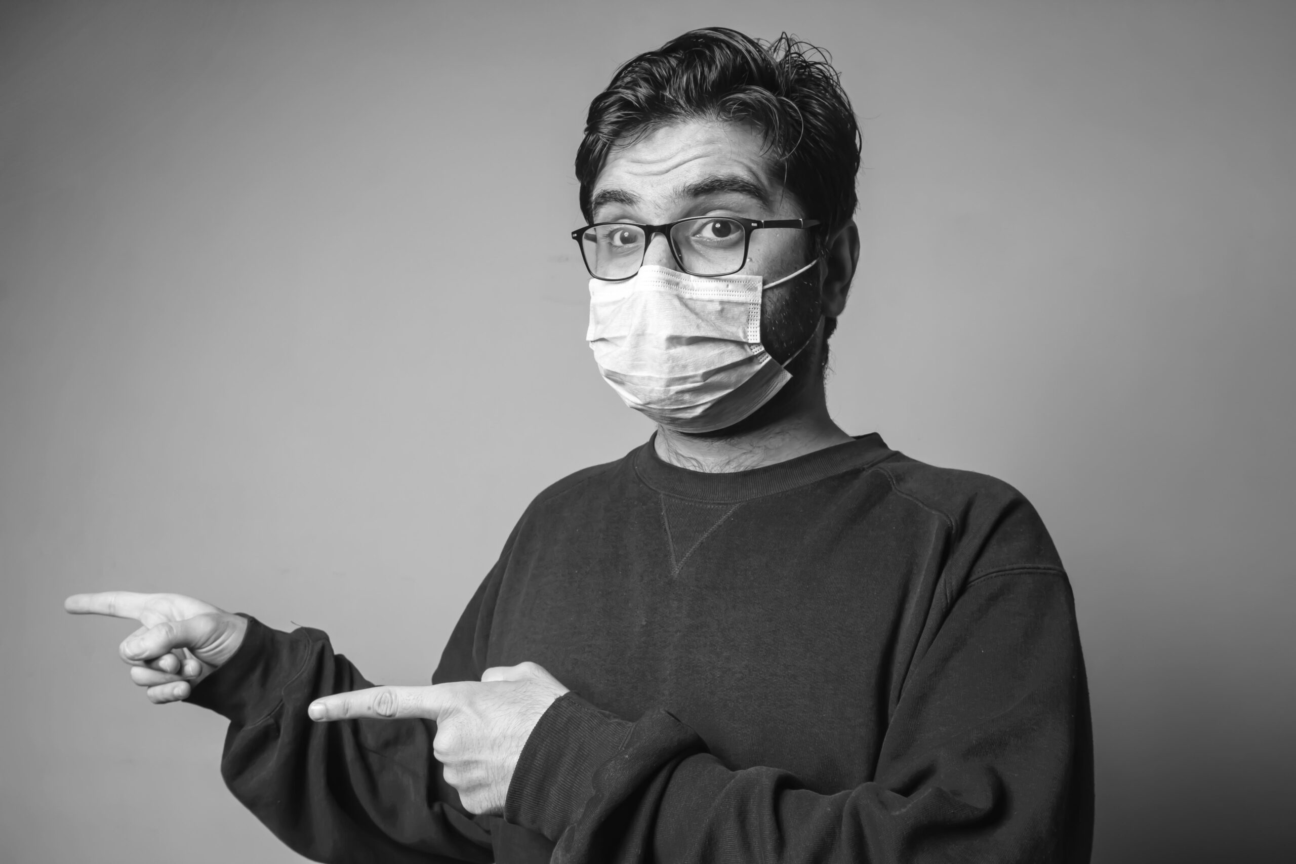 Man wearing face mask pointing at the text to his left.